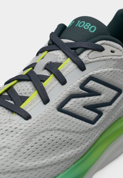 Zapato deportivo gris con cordones oscuros, detalles en verde neón, un gran logo lateral "N" y "1080" en color azul verdoso en la lengüeta negra.