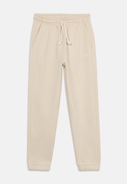 Pantalones jogger de color beige claro con cintura elástica, cordón ajustable, bolsillos laterales y un pequeño logo blanco en el muslo derecho.