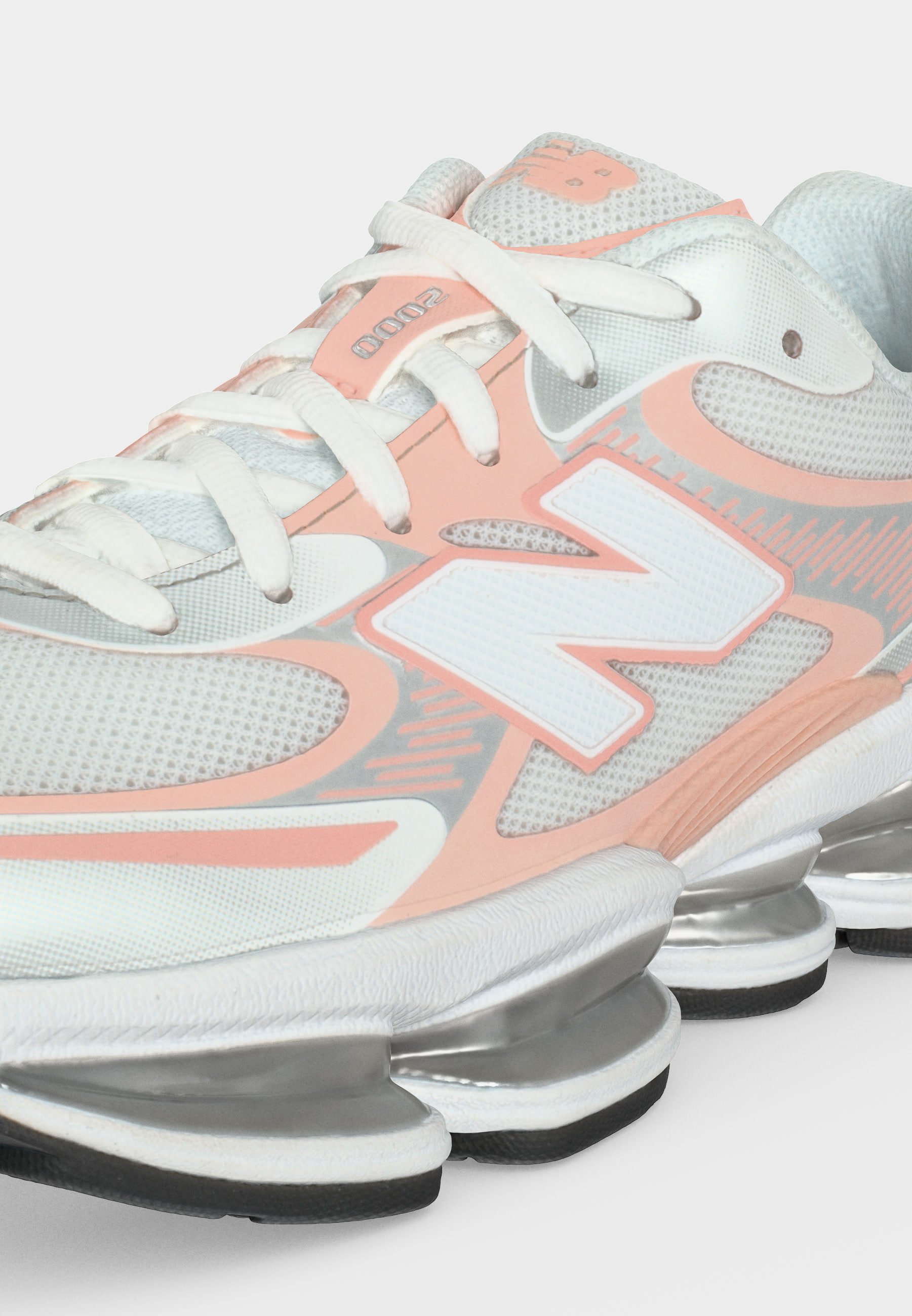 Zapatilla deportiva New Balance blanca y melocotón con tejido de malla, cierre de cordones, gran logotipo "N" y suela plateada segmentada para amortiguación.