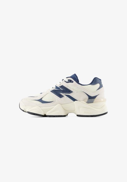 Zapatilla deportiva blanca y azul marino con suela gruesa, parte superior de malla y cuero, y gran logo "N" en el lateral, mostrada desde el lado externo.