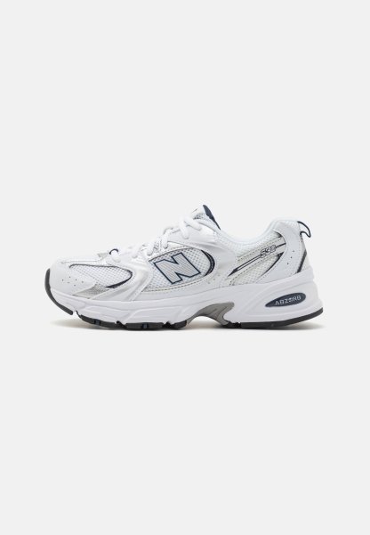 Zapatillas deportivas blancas con parte superior de malla y sintético, que cuentan con una suela acolchada, detalles oscuros y elementos reflectantes cerca del logo.