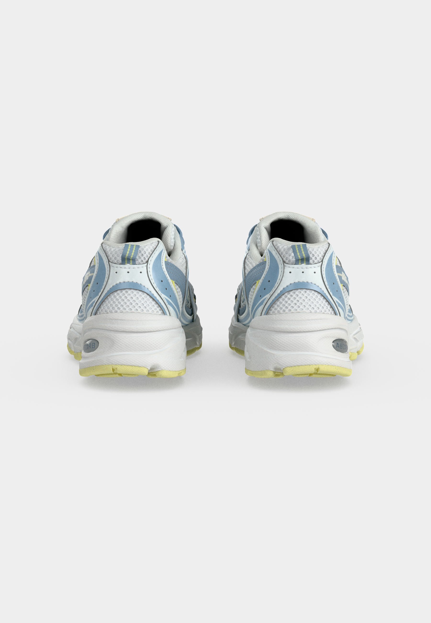 Par de zapatillas deportivas blancas y azules con suelas amarillas vistas desde atrás sobre un fondo liso gris claro.
