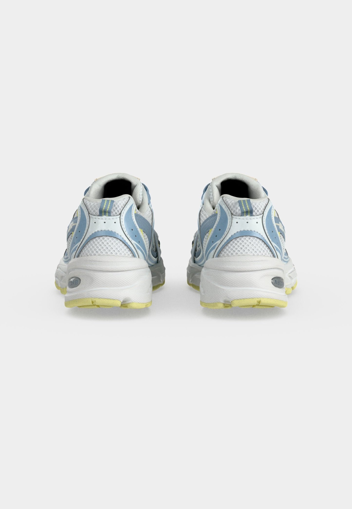 Par de zapatillas deportivas blancas y azules con suelas amarillas vistas desde atrás sobre un fondo liso gris claro.