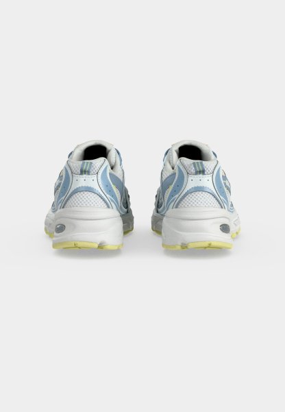 Par de zapatillas deportivas blancas y azules con suelas amarillas vistas desde atrás sobre un fondo liso gris claro.