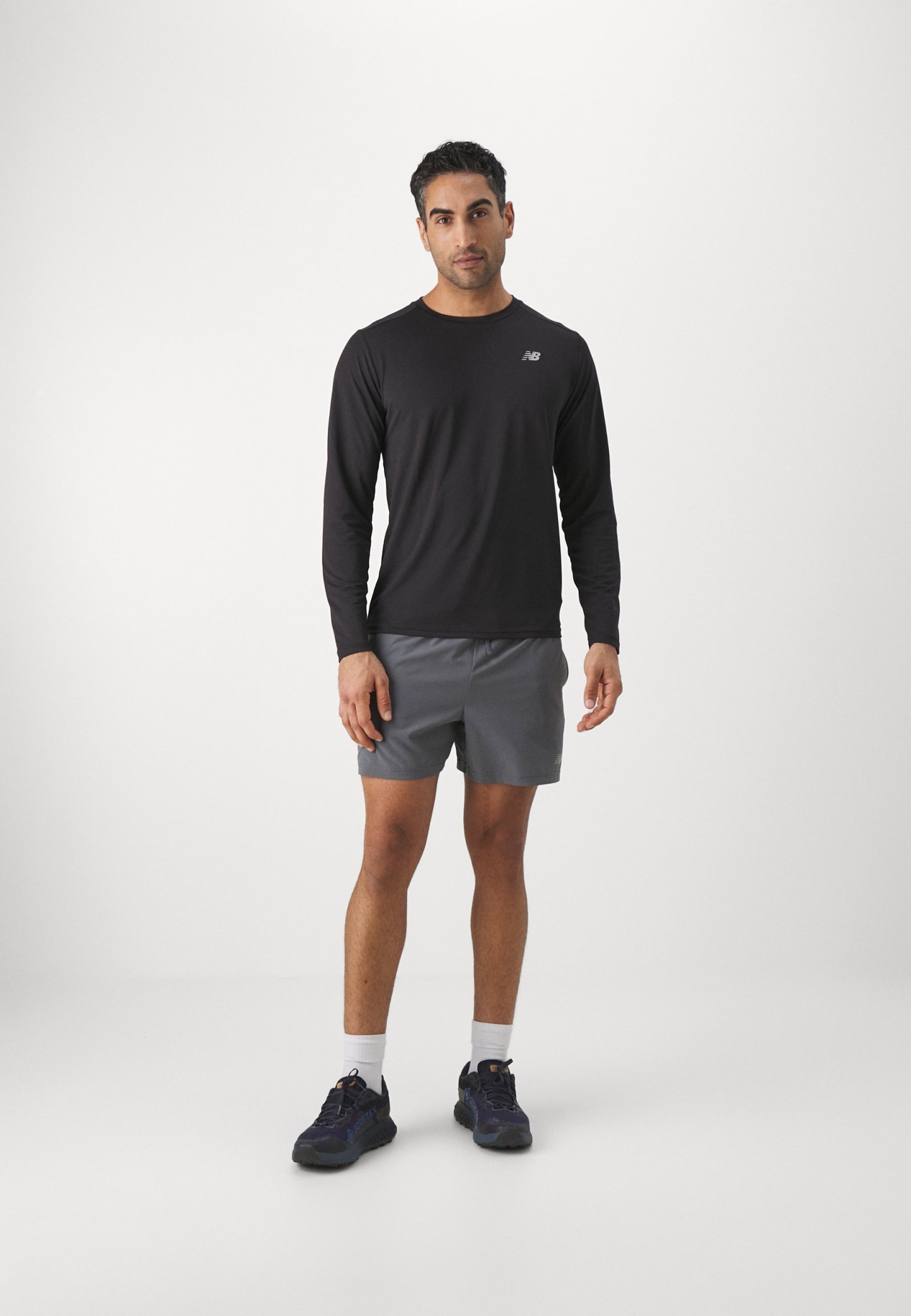 Camisa negra de manga larga con un pequeño logotipo, combinada con pantalones cortos grises. Llevada con zapatillas deportivas oscuras y calcetines blancos hasta el tobillo. Diseño sencillo.
