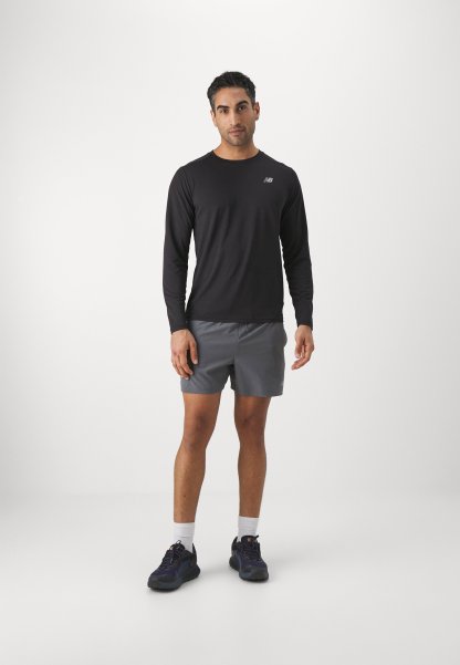 Camisa negra de manga larga con un pequeño logotipo, combinada con pantalones cortos grises. Llevada con zapatillas deportivas oscuras y calcetines blancos hasta el tobillo. Diseño sencillo.