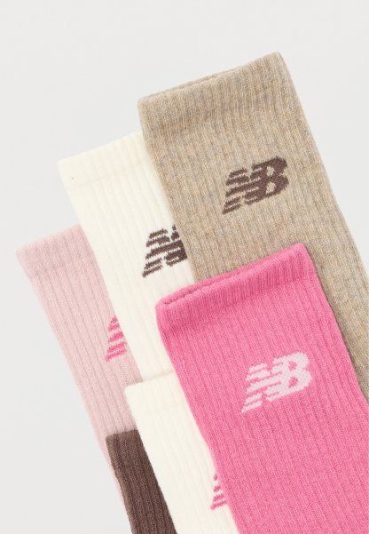Cuatro pares de calcetines acanalados de New Balance en rosa, beige, blanco y rosa claro, cada uno con el logo de la marca en el puño.