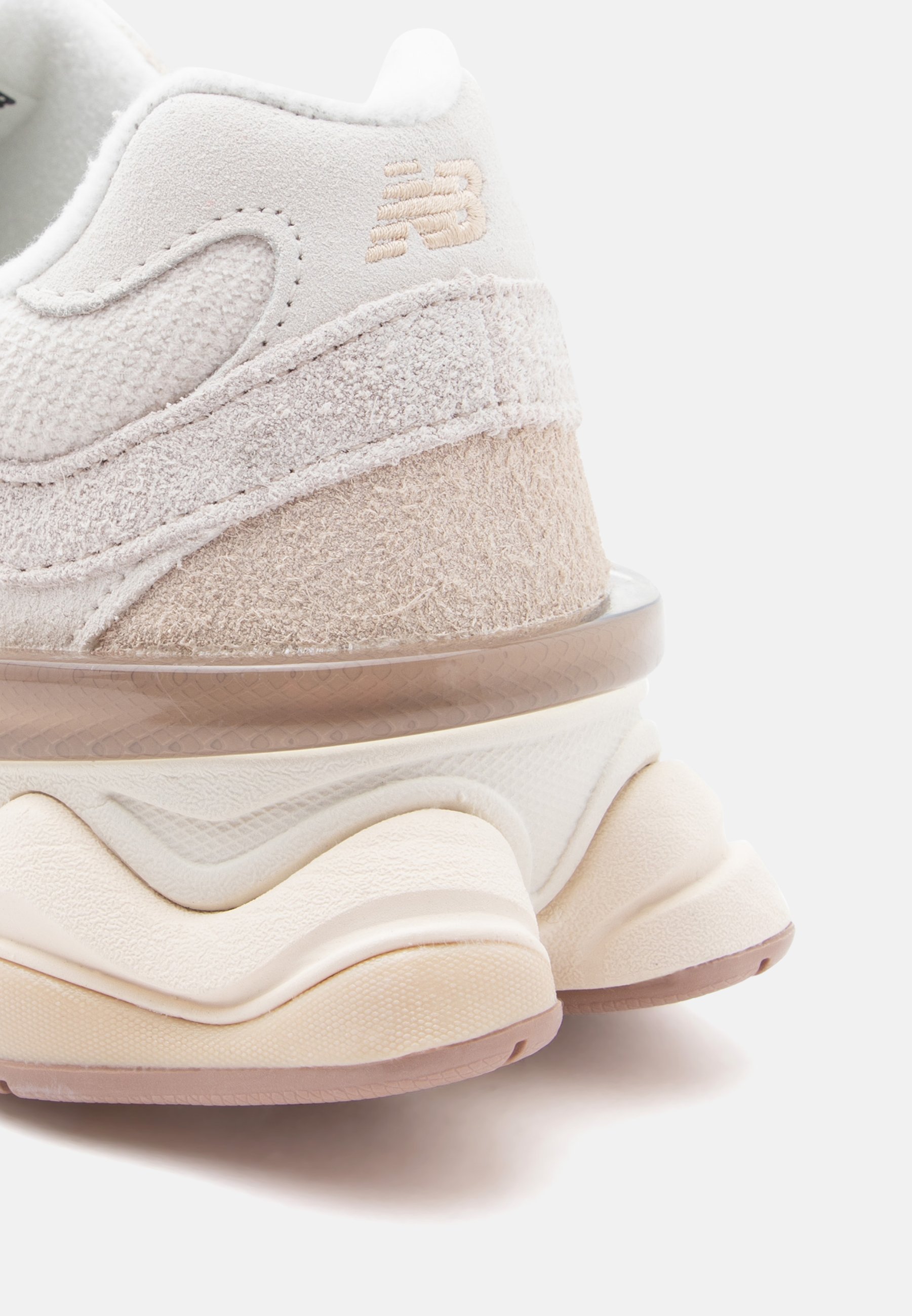 Primer plano del talón de una zapatilla New Balance beige y crema, mostrando gamuza texturizada, entresuela en capas y el logo de la marca bordado en la parte superior.