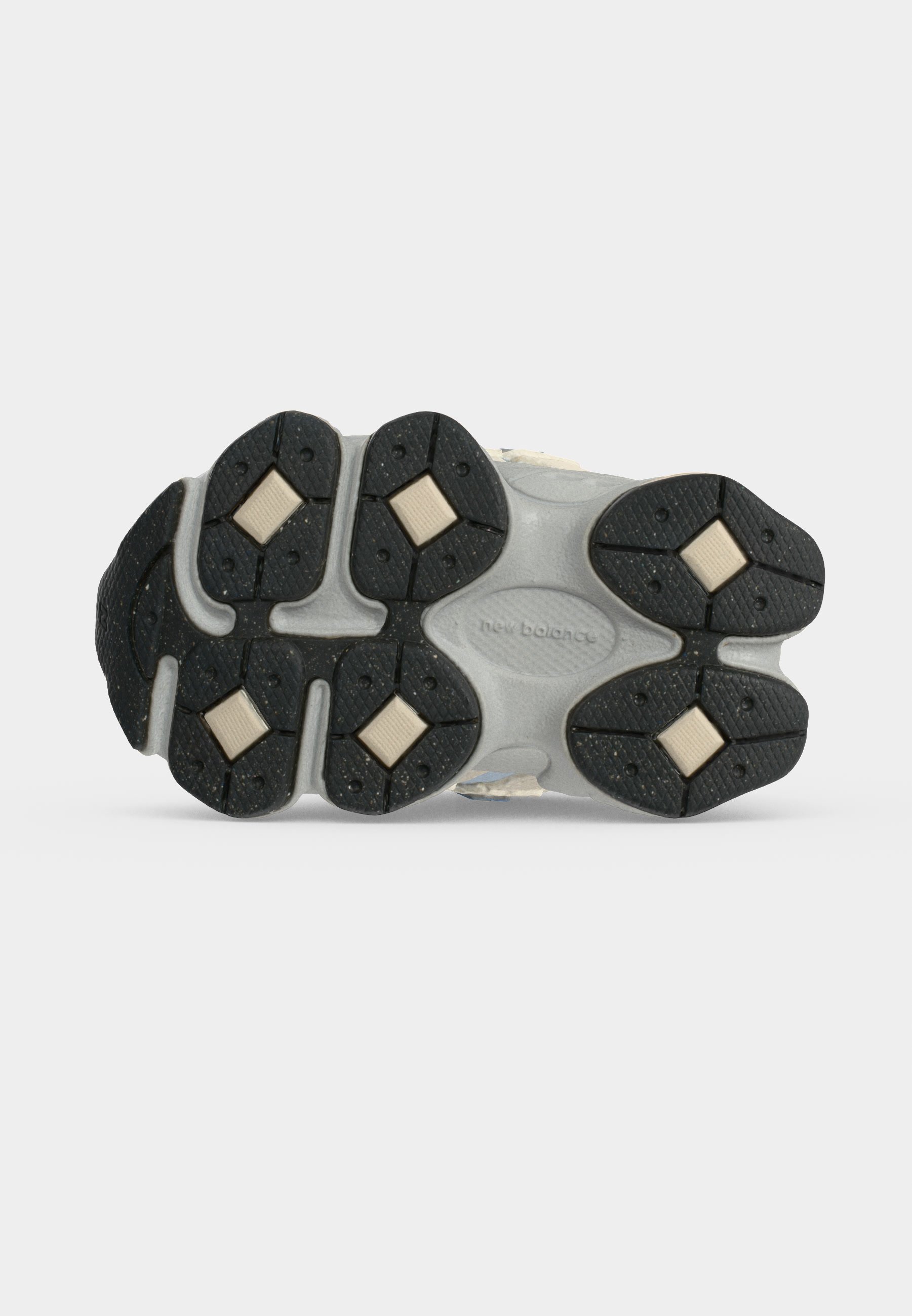 Suela de un zapato New Balance con almohadillas de tracción de goma negra e insertos acolchados beige en forma de diamante sobre fondo blanco.
