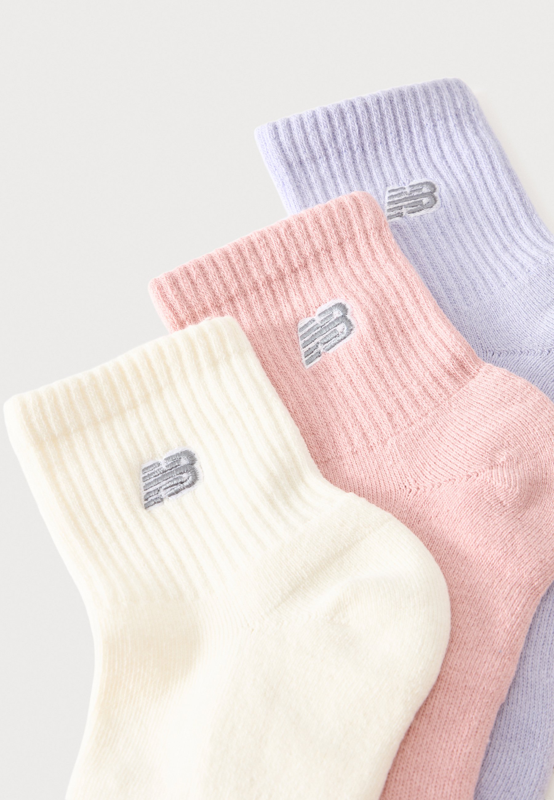 Tres calcetines tobilleros acanalados en crema, rosa y lila claro, cada uno con un pequeño logo gris bordado cerca del puño.