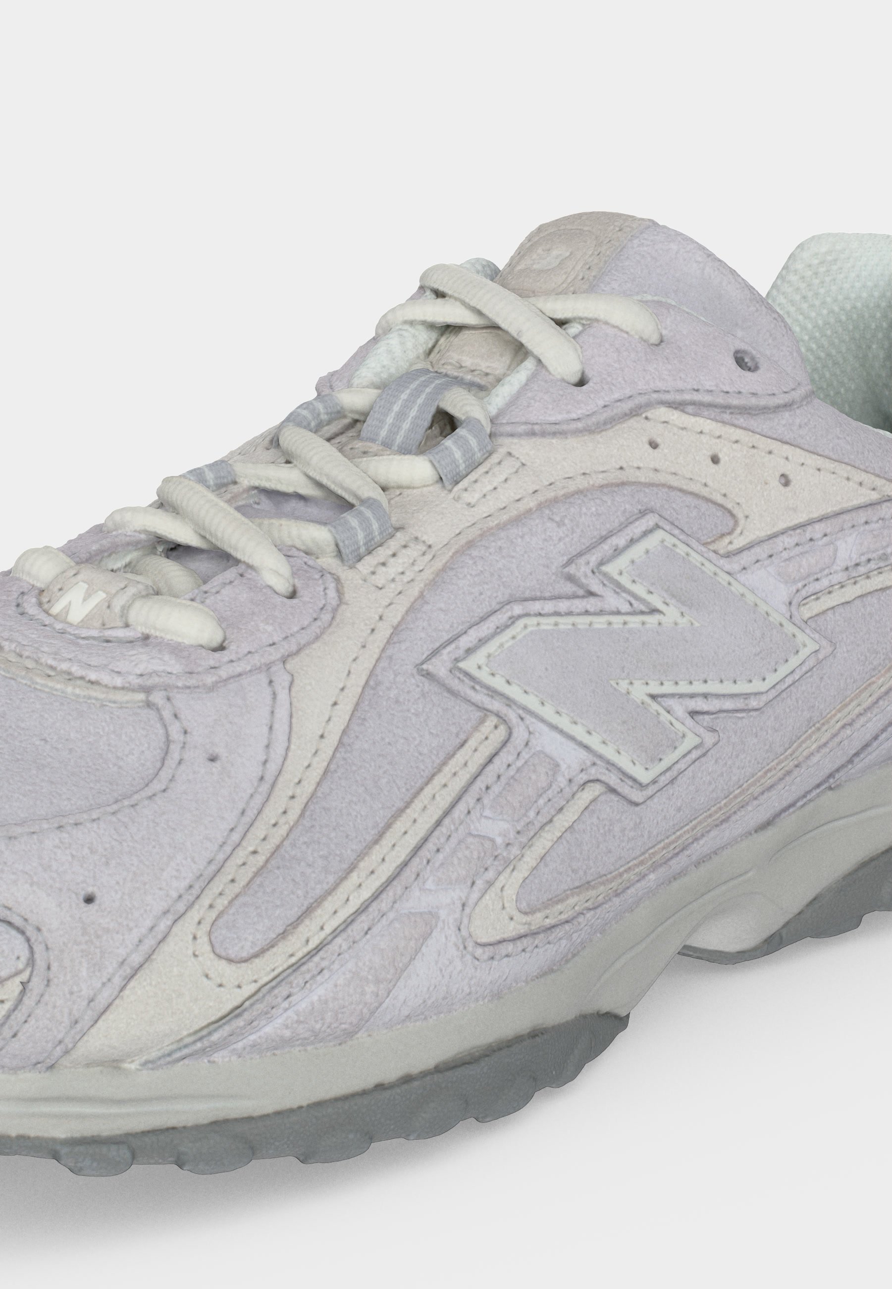 Zapatilla deportiva de ante gris claro con cordones blancos, cuello acolchado y un gran logo "N" cosido en el lateral, sobre una suela de goma gris.