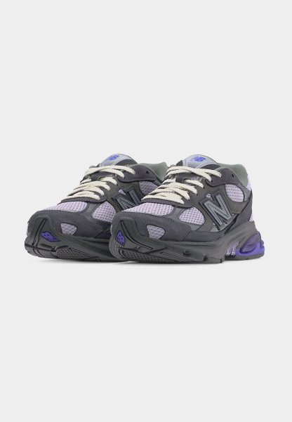 Par de zapatillas New Balance en tonos gris y morado con cordones blancos, tejido de malla y suelas acolchadas sobre un fondo blanco.