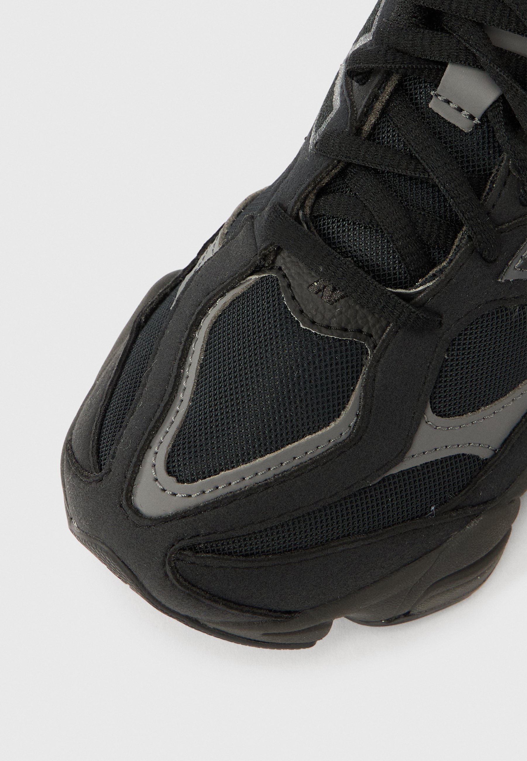 Zapatilla deportiva negra con parte superior de malla y tela texturizada, con detalles en gris y una suela gruesa de goma, diseñada para brindar comodidad y transpirabilidad.