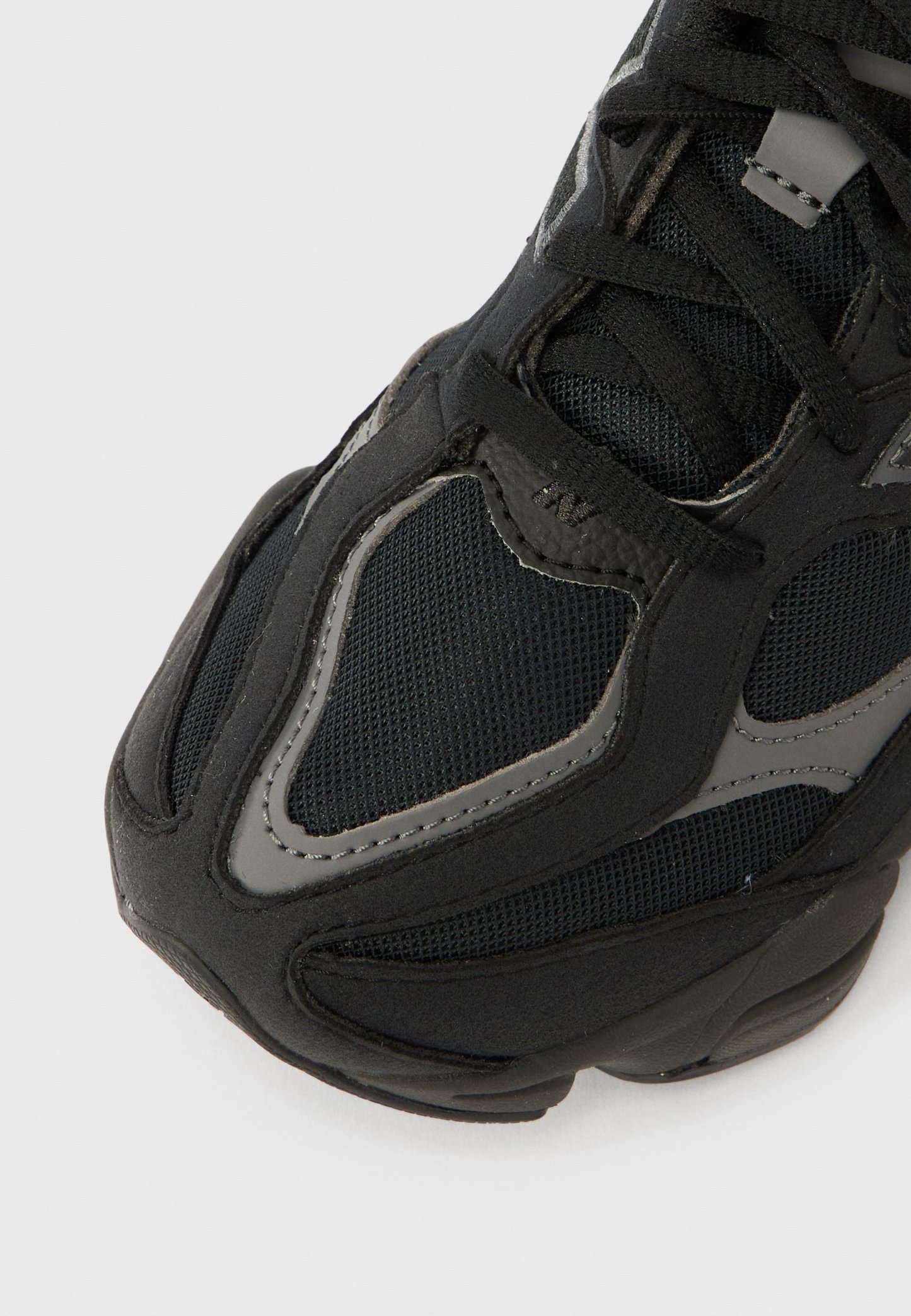 Zapatilla deportiva negra con parte superior de malla y tela texturizada, con detalles en gris y una suela gruesa de goma, diseñada para brindar comodidad y transpirabilidad.