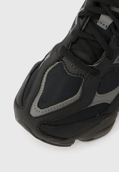 Zapatilla deportiva negra con parte superior de malla y tela texturizada, con detalles en gris y una suela gruesa de goma, diseñada para brindar comodidad y transpirabilidad.