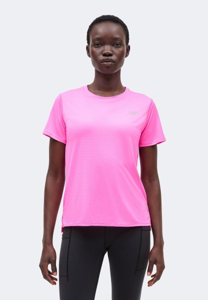 Mujer de pie con una camiseta deportiva de manga corta de color rosa brillante y pantalones negros ajustados, mirando al frente con expresión neutral.