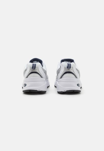 Zapatillas deportivas blancas con un upper de malla transpirable, detalles en gris, un cuello acolchado y suelas de goma texturizadas. Presentan un diseño curvado.