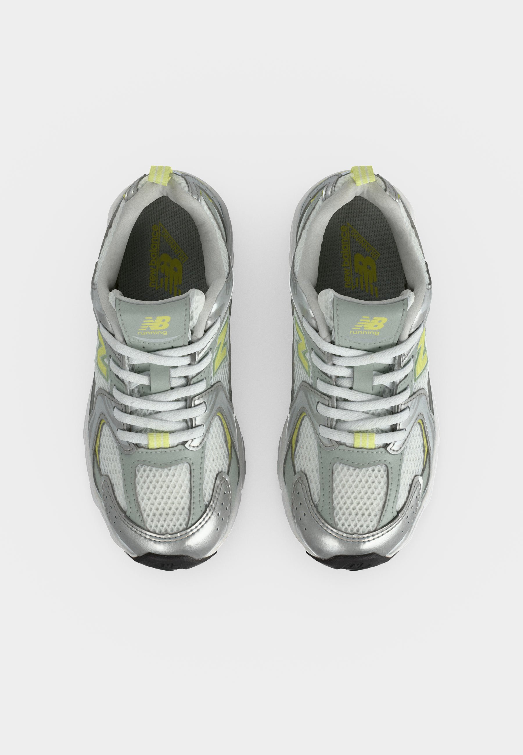 Par de zapatillas de running New Balance plateadas y grises con cordones blancos y detalles en amarillo claro vistas desde arriba sobre fondo blanco.