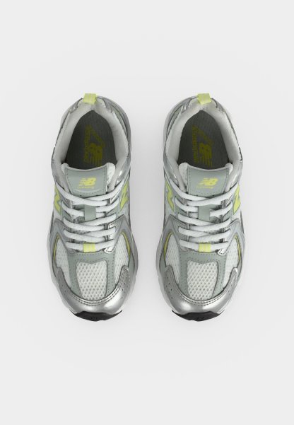 Par de zapatillas de running New Balance plateadas y grises con cordones blancos y detalles en amarillo claro vistas desde arriba sobre fondo blanco.
