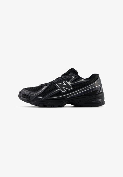 Zapatilla deportiva negra con parte superior de malla, suela de goma y detalles texturizados. El diseño incluye un logotipo plateado prominente y acentos en contraste.