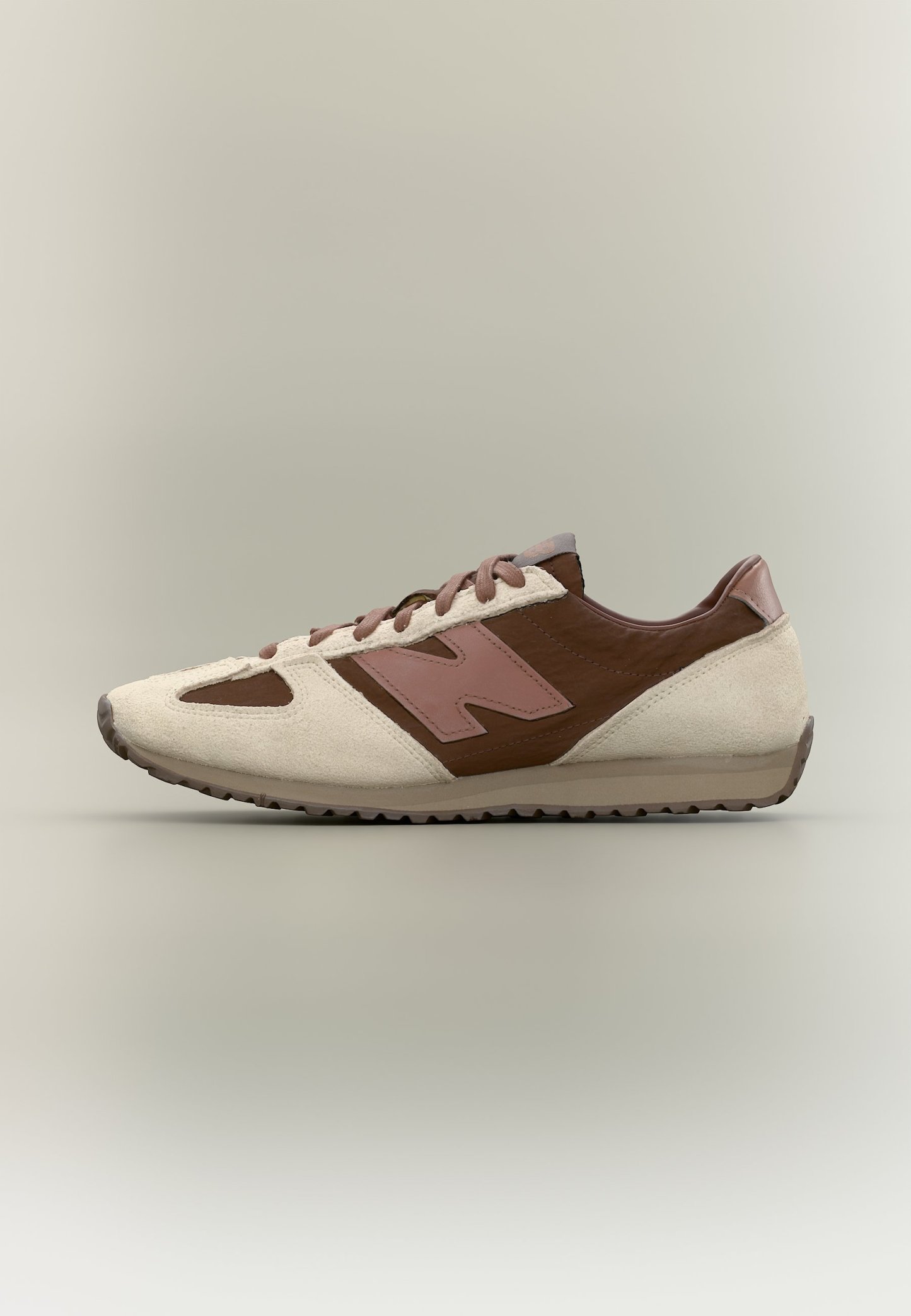 Zapatilla baja beige y marrón con paneles de ante y cuero, cordones marrones y suela de goma texturizada, mostrada de lado sobre un fondo neutro.