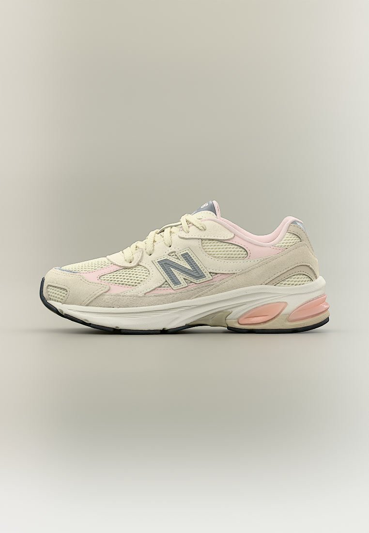 Zapatilla New Balance beige y rosa con paneles de malla y ante, logo gris, suela acolchada y suela exterior negra, vista desde un lateral.