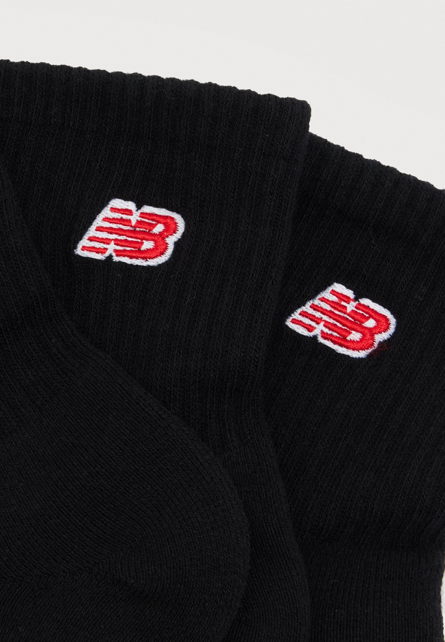 Calcetines negros de punto acanalado con logotipos "NB" bordados en rojo y blanco en los puños, mostrados extendidos sobre un fondo blanco.