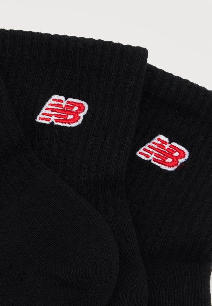 Calcetines negros de punto acanalado con logotipos "NB" bordados en rojo y blanco en los puños, mostrados extendidos sobre un fondo blanco.