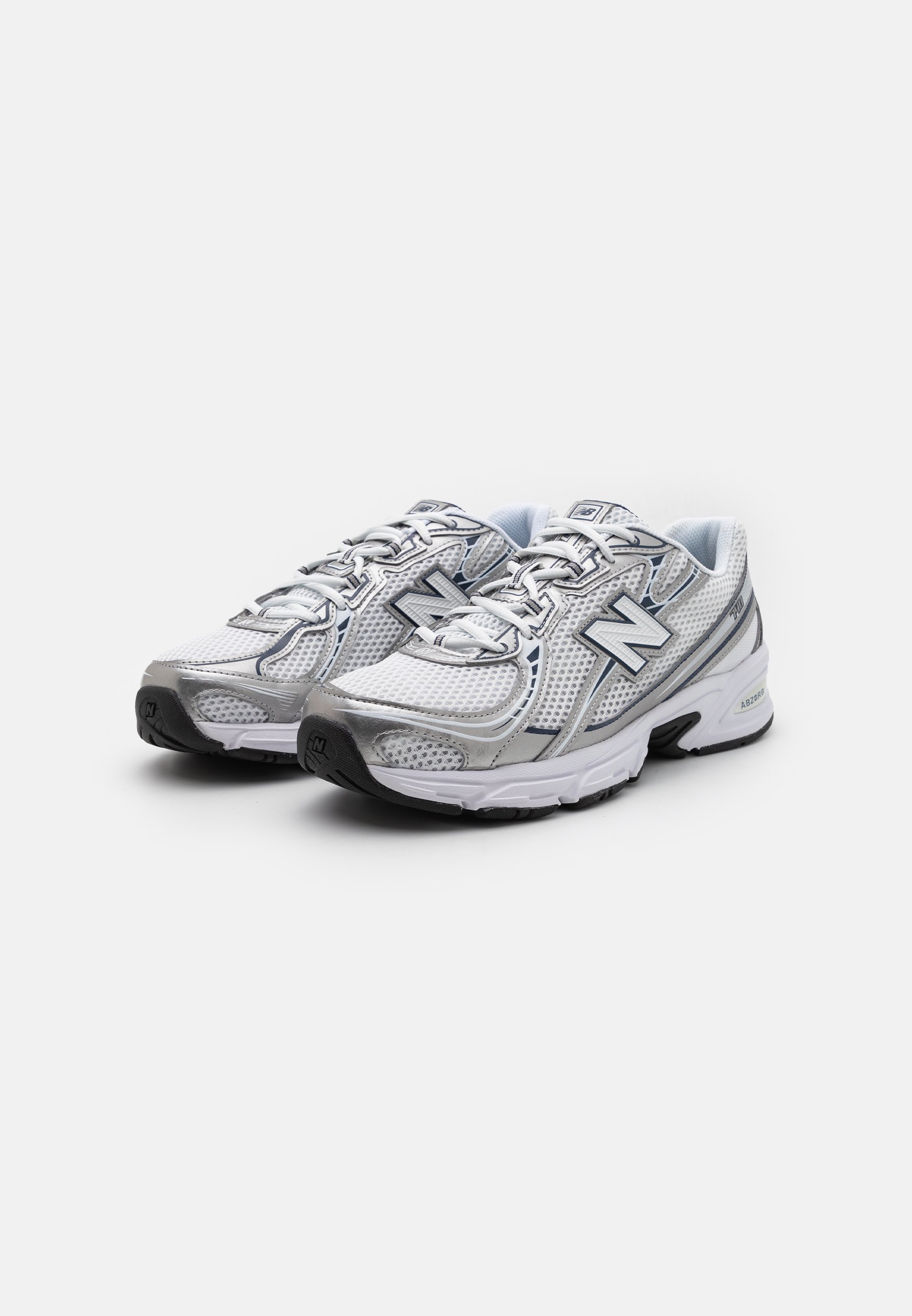 Zapatillas deportivas blancas y plateadas con parte superior de malla, puntera redondeada, diseño de cordones, cuello acolchado y suela de goma con una banda de rodadura texturizada.