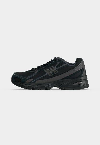 Zapatilla de running New Balance negra y gris oscuro con cierre de cordones y suela acolchada, mostrada de perfil sobre un fondo claro y liso.