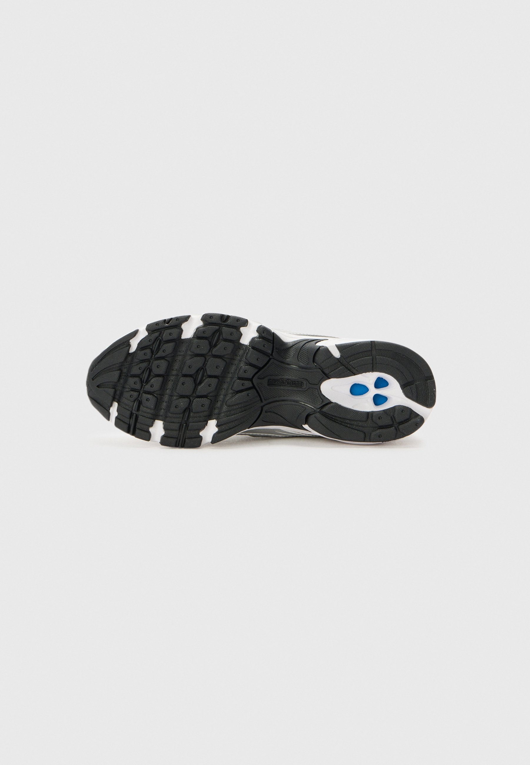Suela de zapatilla en blanco y negro con dibujo de banda de rodadura texturizada e insertos acolchados azules, mostrada desde abajo sobre un fondo sencillo.