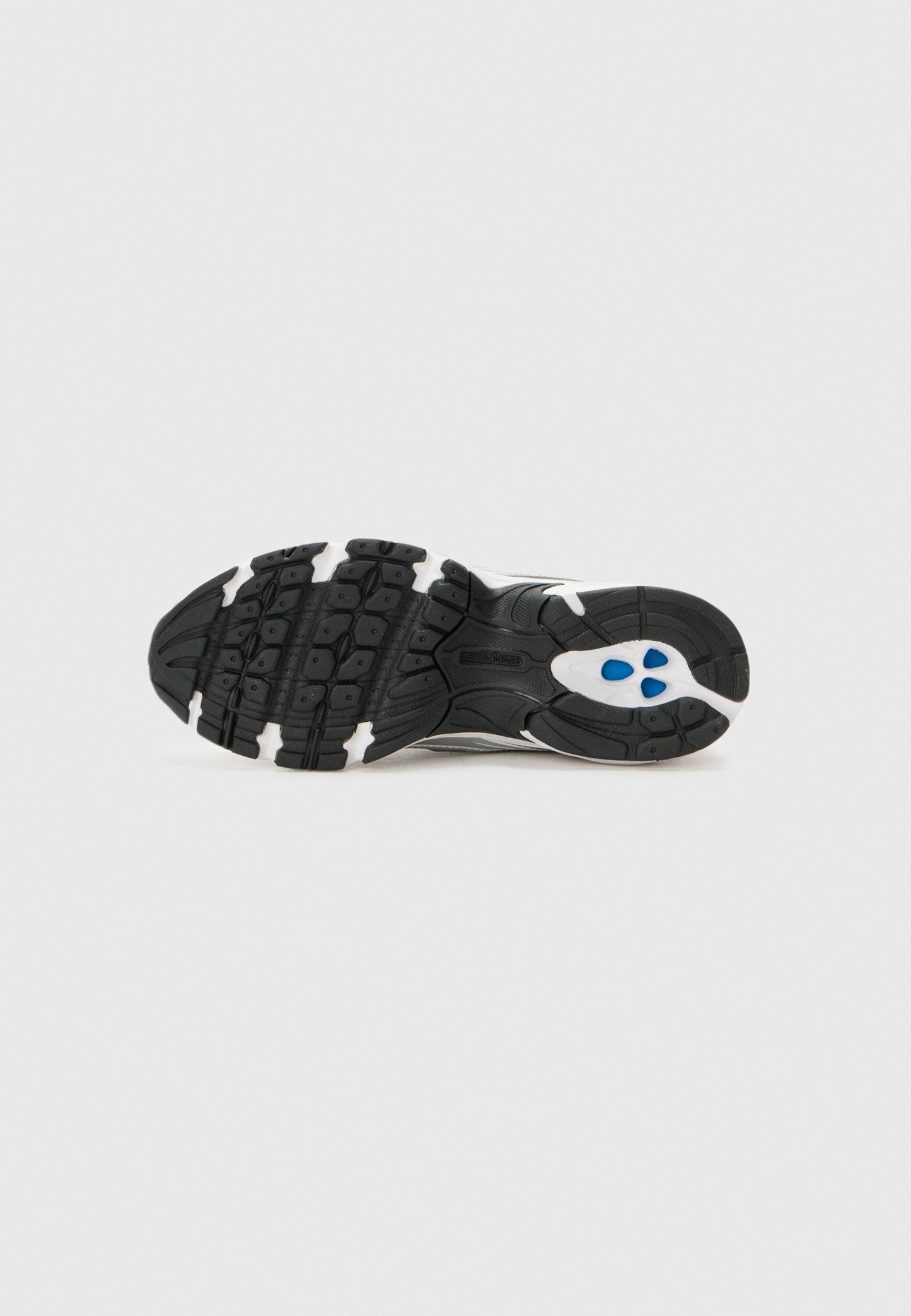 Suela de zapatilla en blanco y negro con dibujo de banda de rodadura texturizada e insertos acolchados azules, mostrada desde abajo sobre un fondo sencillo.