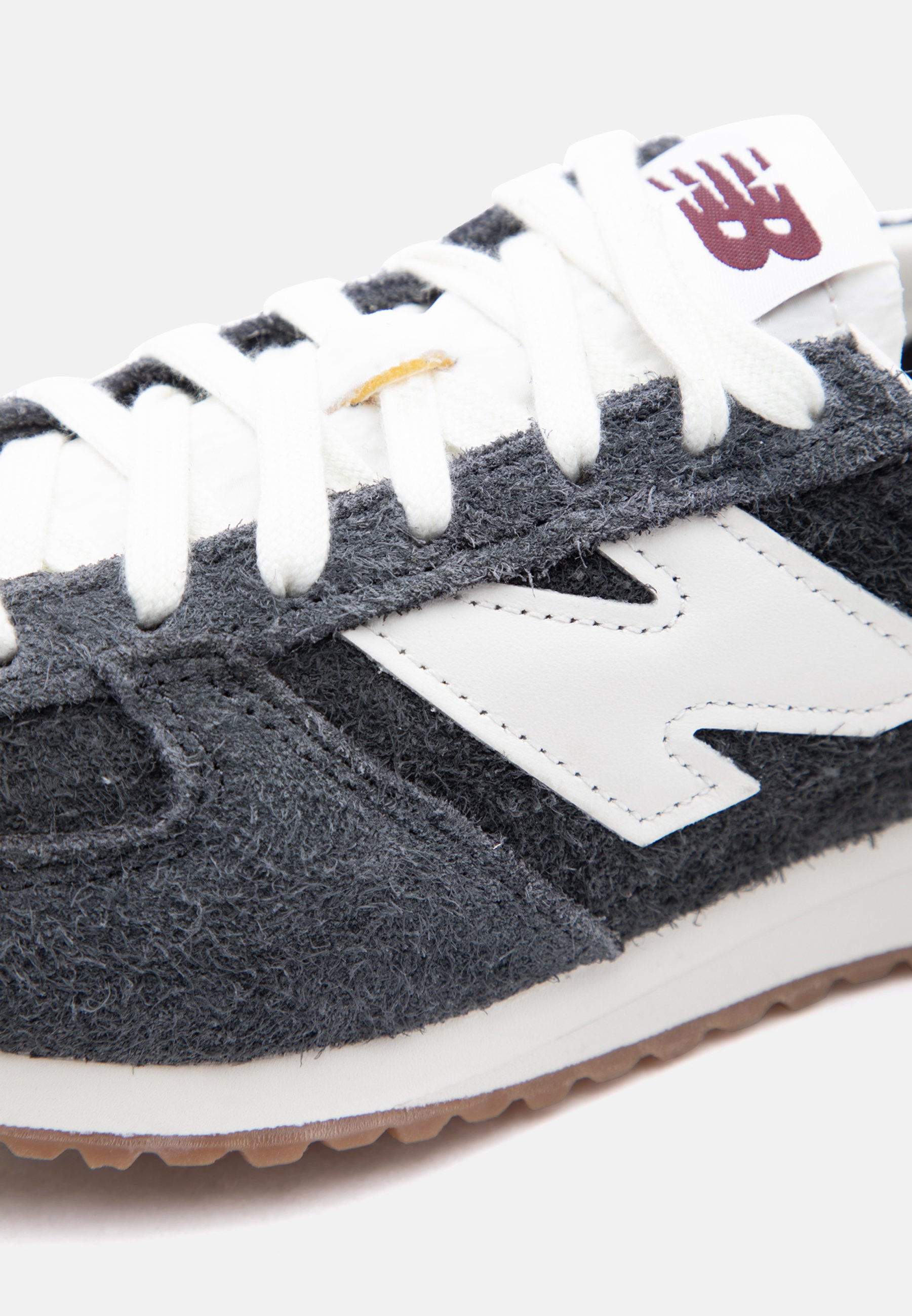 Primer plano de una zapatilla New Balance gris y blanca con cordones blancos y una suela marrón de goma.