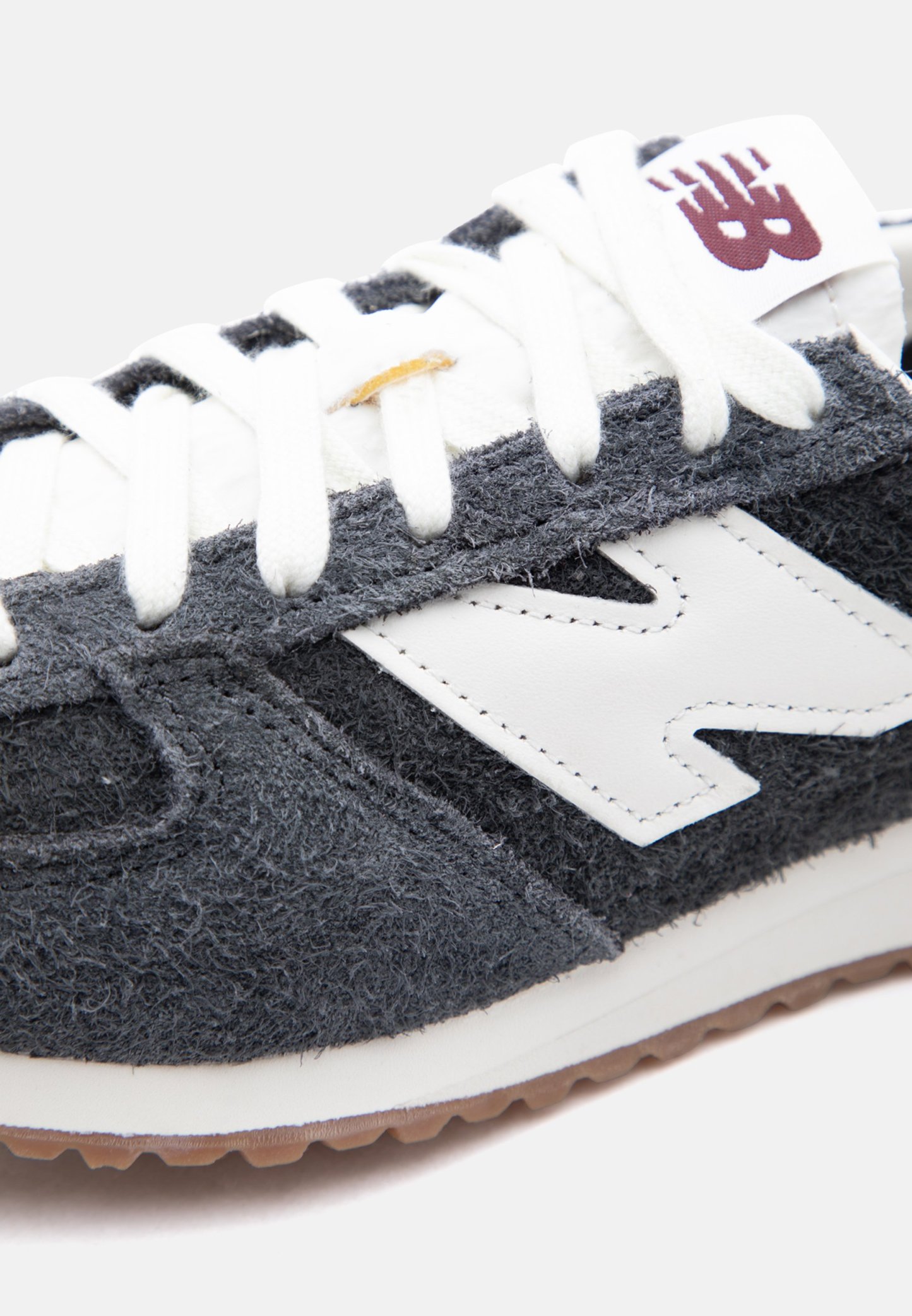 Primer plano de una zapatilla New Balance gris y blanca con cordones blancos y una suela marrón de goma.