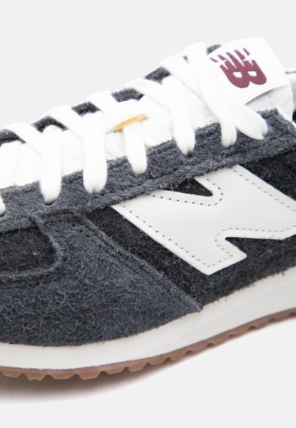 Primer plano de una zapatilla New Balance gris y blanca con cordones blancos y una suela marrón de goma.