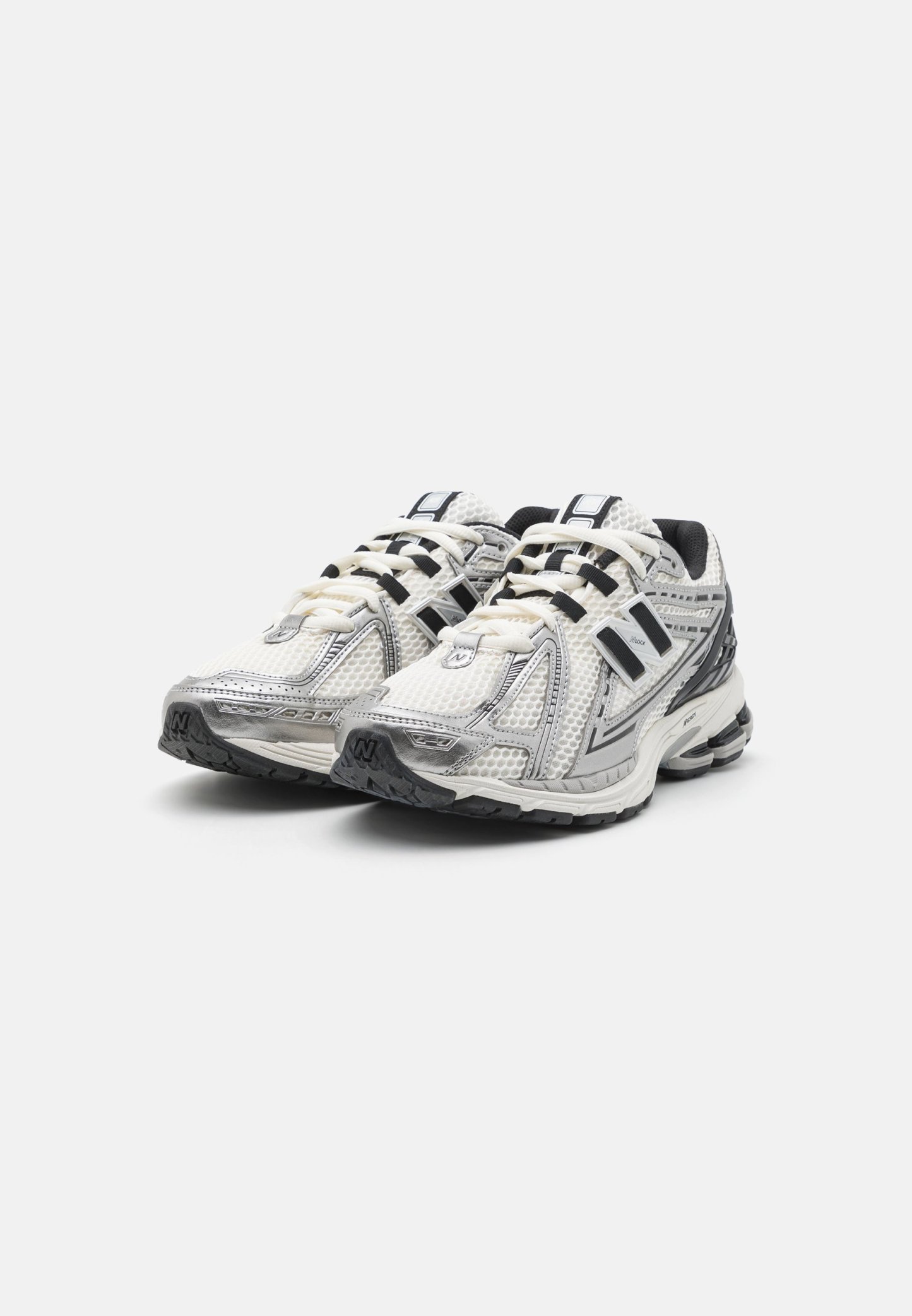 Zapatillas deportivas con parte superior de malla en blanco y gris, con acentos negros, cordones gruesos y una suela de goma texturizada para mayor tracción.