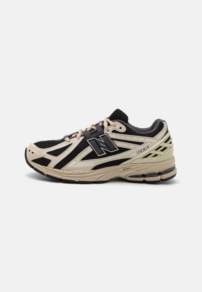 Zapatilla de correr New Balance 1906R en negro y beige, con parte superior de malla, suela gruesa acolchada y cierre de cordones, mostrada de perfil.