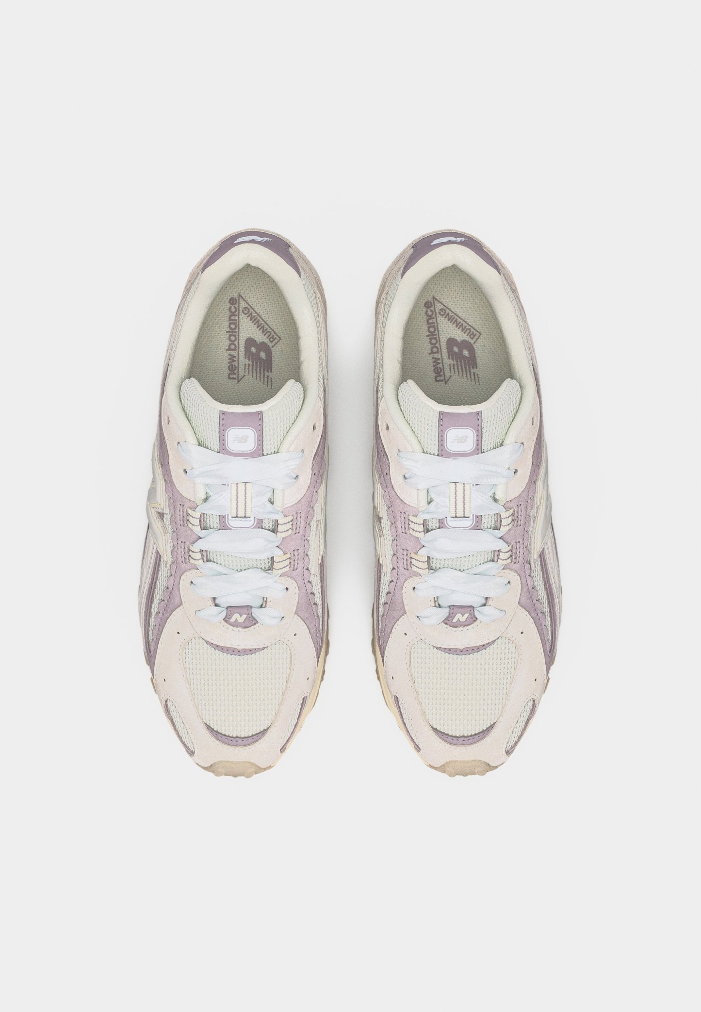 Par de zapatillas para correr New Balance en rosa claro y beige con cordones blancos, vista desde arriba sobre un fondo blanco.