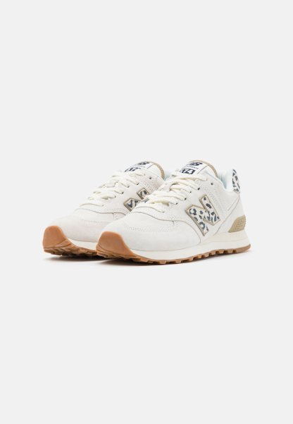Par de zapatillas de color blanco roto con suelas de goma y detalles con estampado de leopardo en el logo y la lengüeta del talón, colocadas lado a lado sobre un fondo blanco.