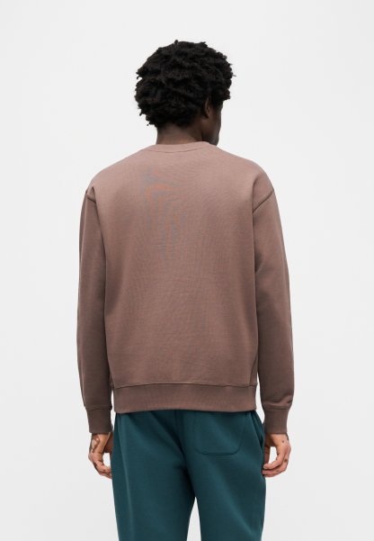 Sudadera marrón con cuello y puños acanalados, de corte holgado y textura suave, combinada con pantalones verde azulado.