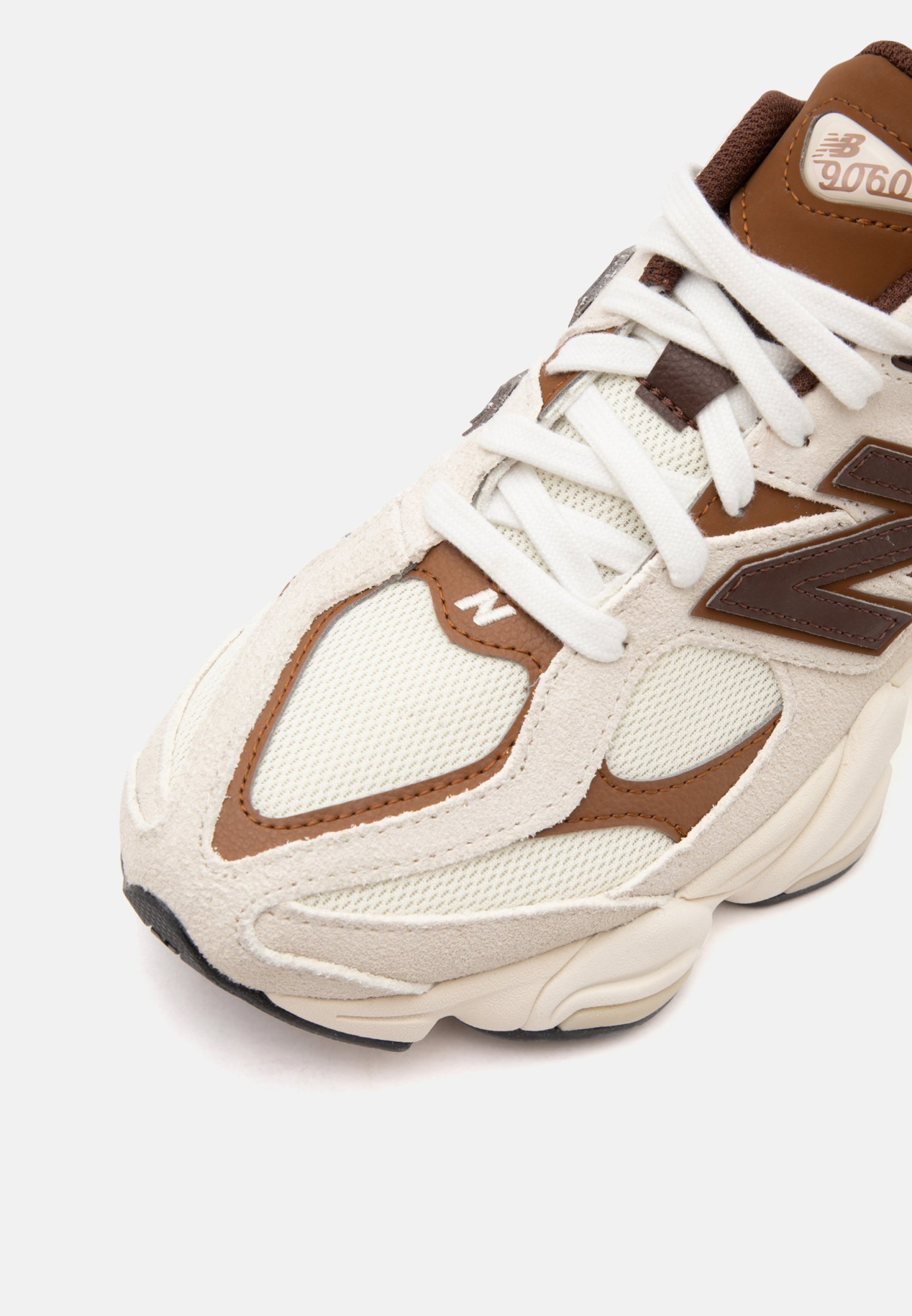Primer plano de una zapatilla New Balance 9060 beige y marrón con cordones blancos y parte superior de tela de malla.