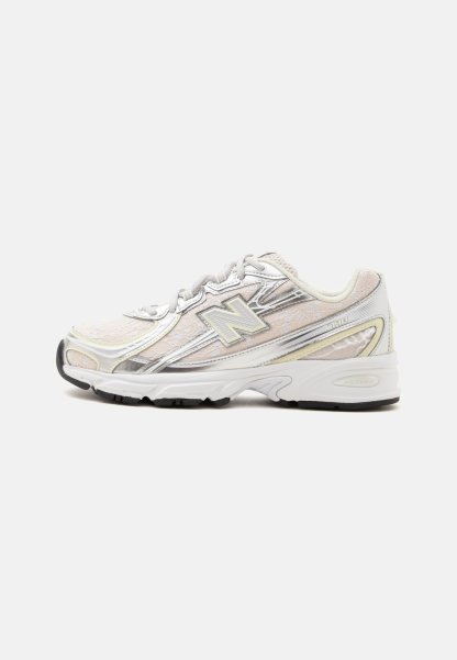 Zapatilla de running New Balance blanca y plateada con cordones delanteros, tejido de malla y suela de goma negra vista desde un lateral.
