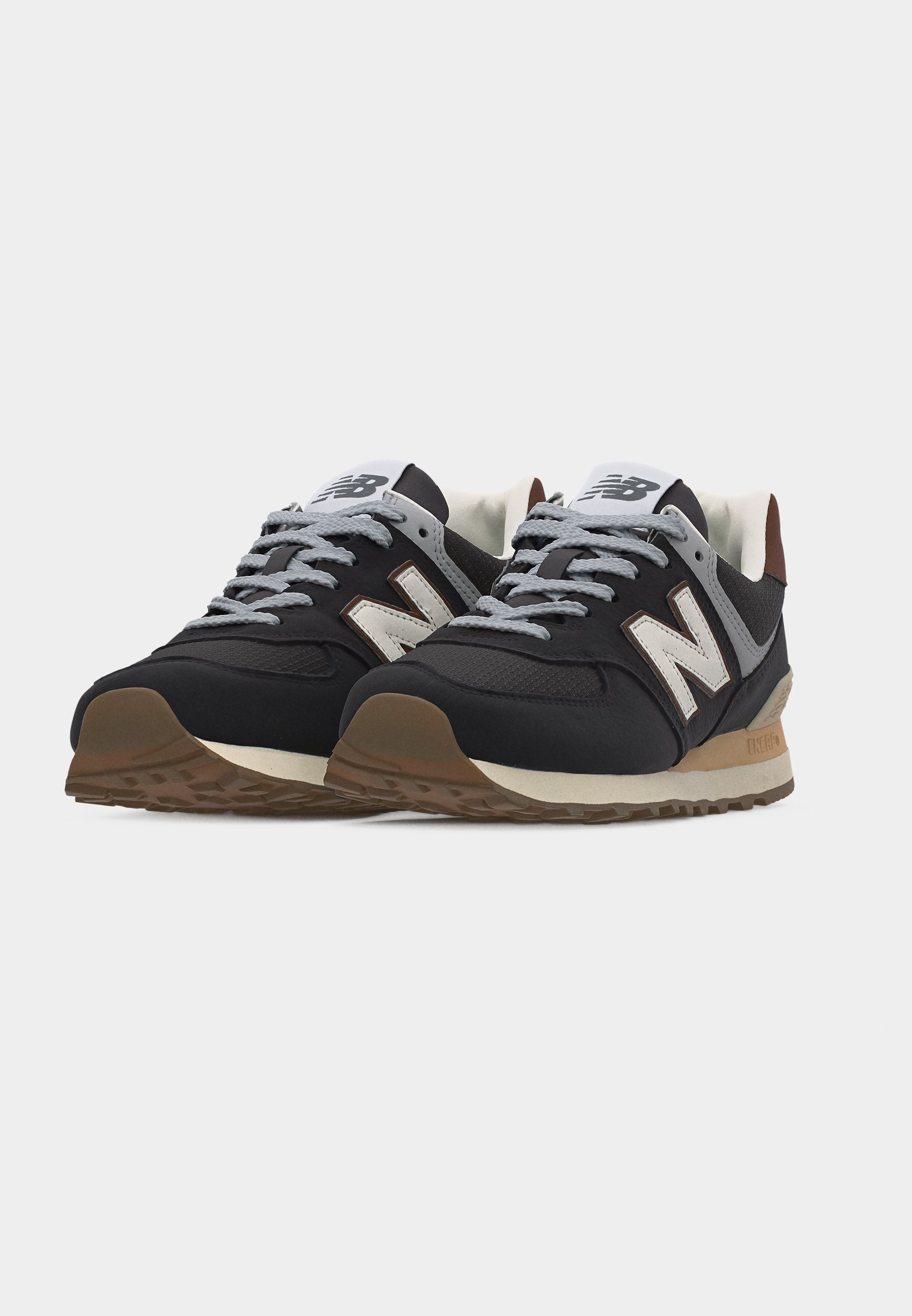 Par de zapatillas New Balance en negro y gris con el logo "N" blanco, cordones grises y suelas color beige, dispuestas en un ángulo sobre un fondo blanco.