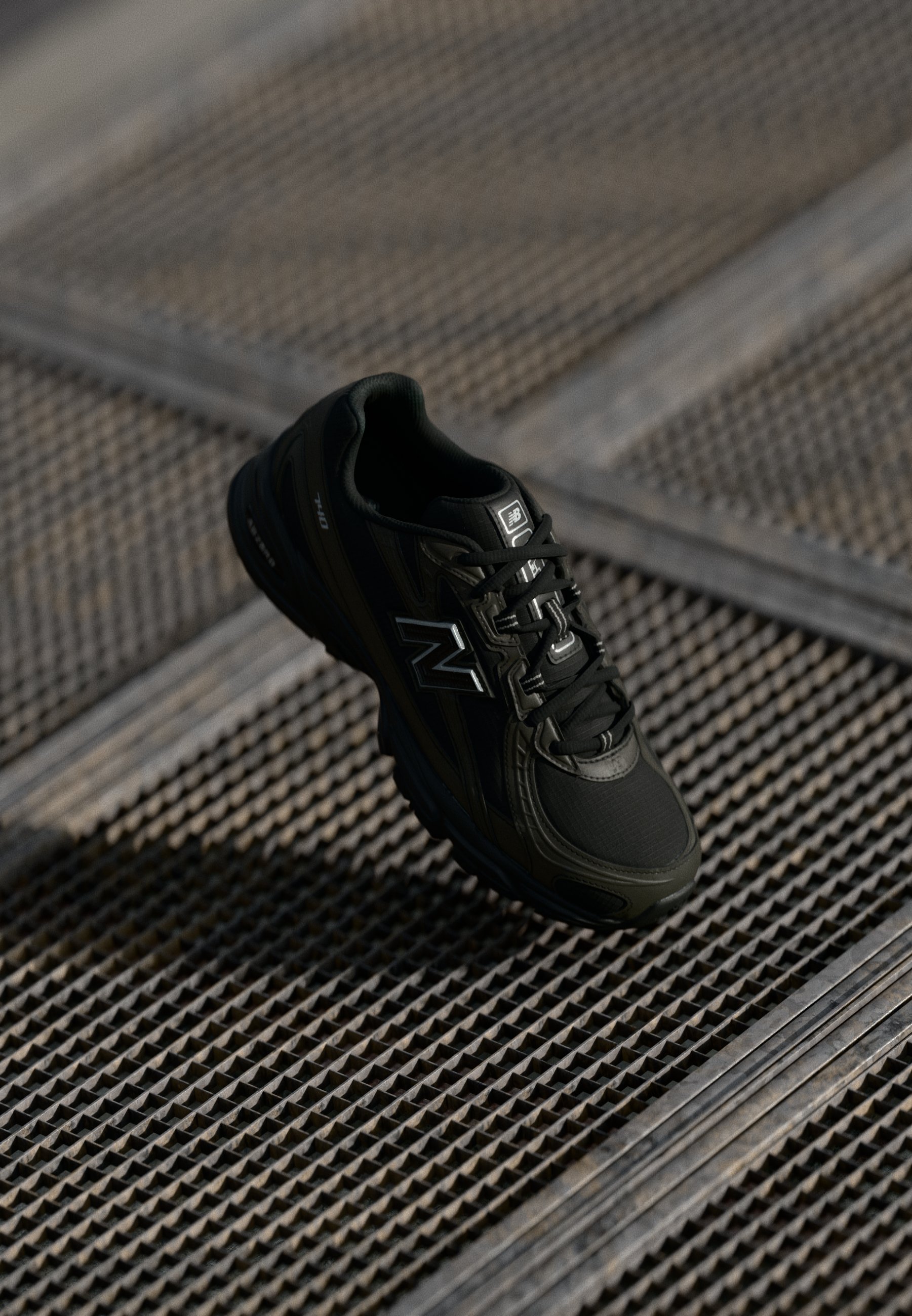 Zapatilla deportiva negra con tejido texturizado, superposiciones sintéticas y cordones. Presenta una suela gruesa y un acento de logo reflectante.