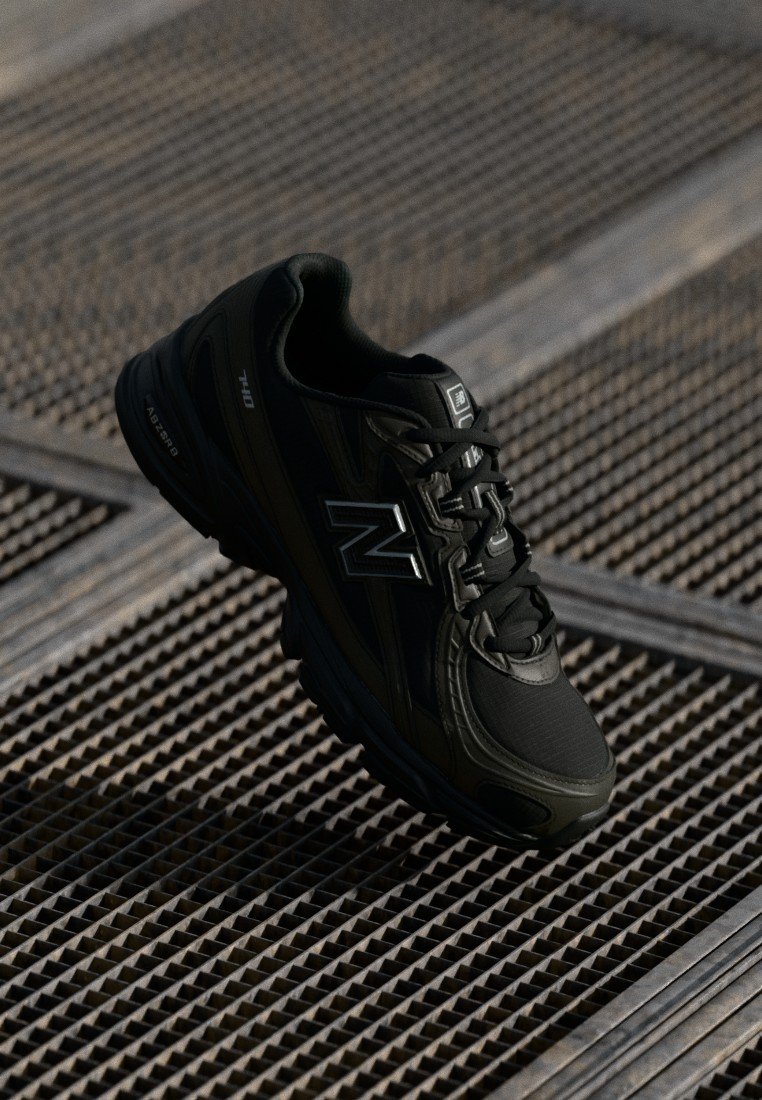 Zapatilla deportiva negra con un upper sintético texturizado, diseño de cordones y acentos plateados, que cuenta con una suela acolchada y una silueta moderna.