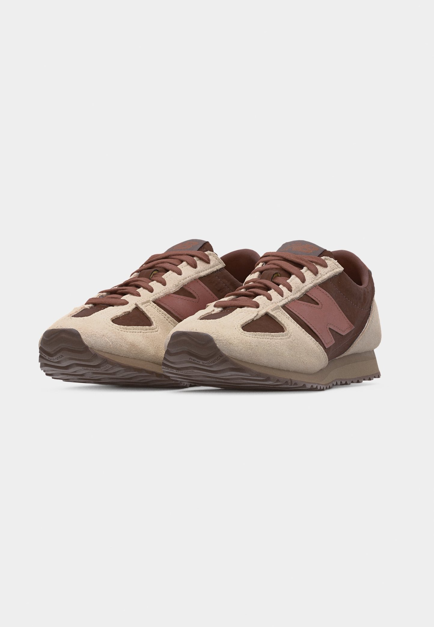 Par de zapatillas New Balance en tonos marrón y beige con paneles de ante y cuero, cierre de cordones y suelas de goma texturizadas.