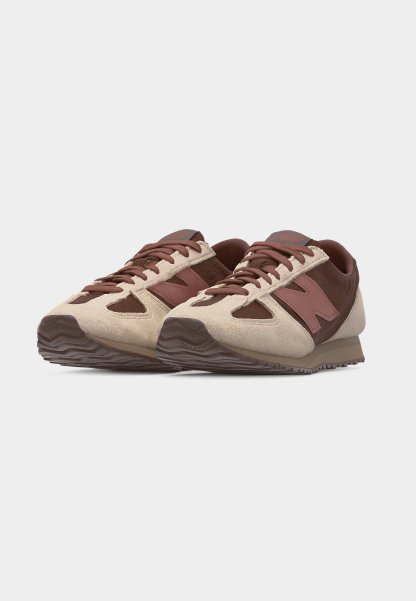 Par de zapatillas New Balance en tonos marrón y beige con paneles de ante y cuero, cierre de cordones y suelas de goma texturizadas.