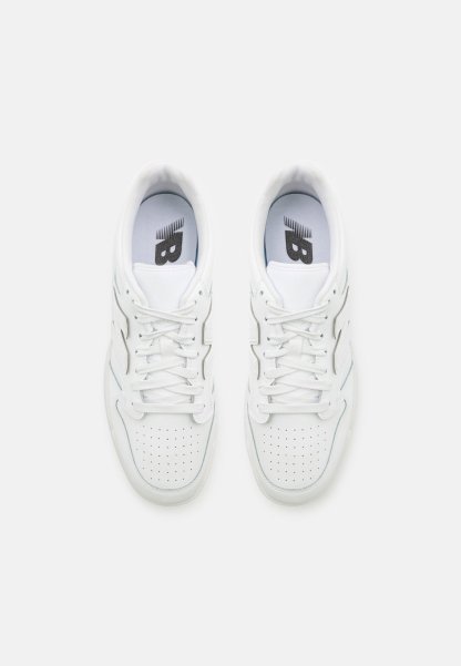 Zapatillas blancas con una parte superior de cuero suave, puntera perforada para transpirabilidad, cordones planos y un logo en la lengüeta. Diseño minimalista.