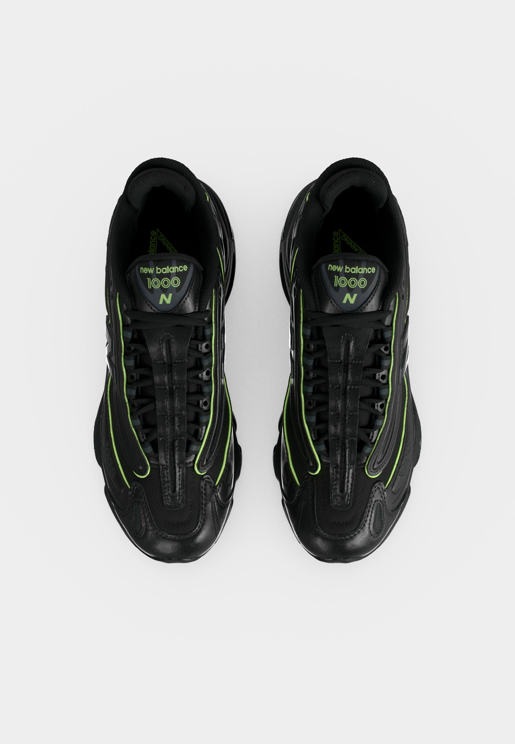 Par de zapatillas negras New Balance 1000 con detalles en verde neón, vista desde arriba sobre un fondo blanco.