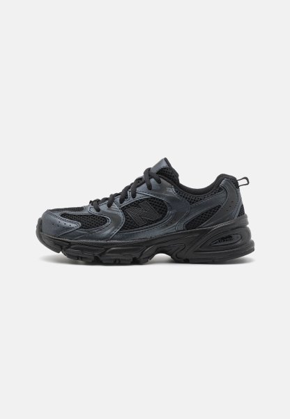 Zapatilla deportiva negra con paneles de malla y acentos sintéticos suaves. Cuenta con una suela de goma gruesa y un cierre de cordones para un ajuste seguro.